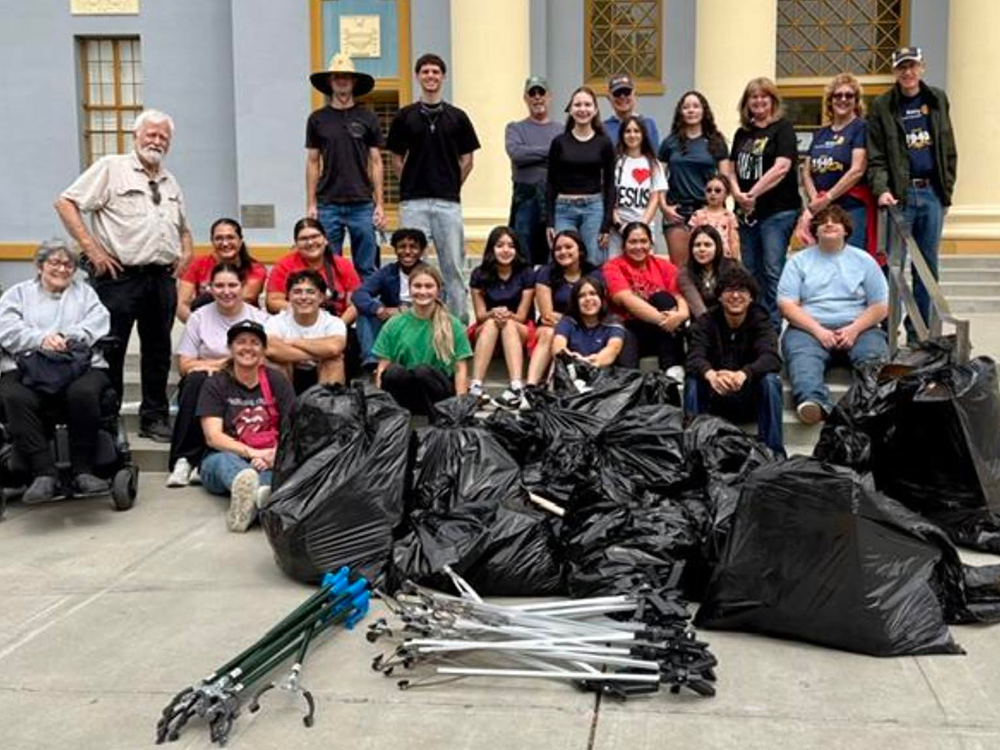Group photo of Interact students and Hanford Rotarians on steps of Civic Auditorium. Full trash bags are piled in front of them along with trash grabbers.
