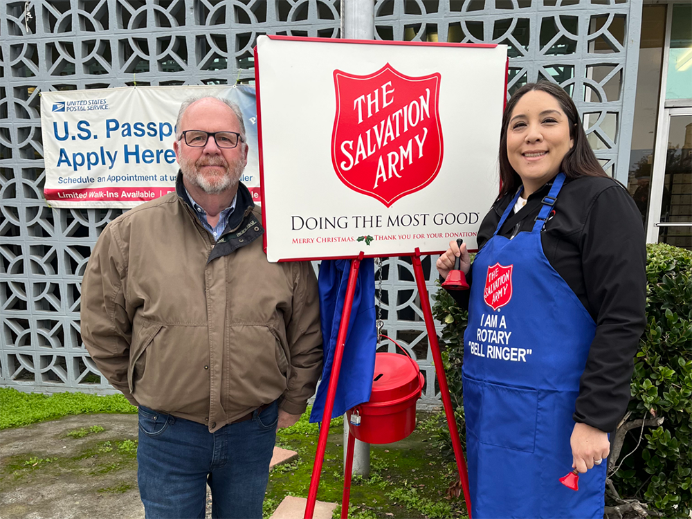 Mark York and Maritza Lemos stand smiling with a Salvation Army bell and sign.